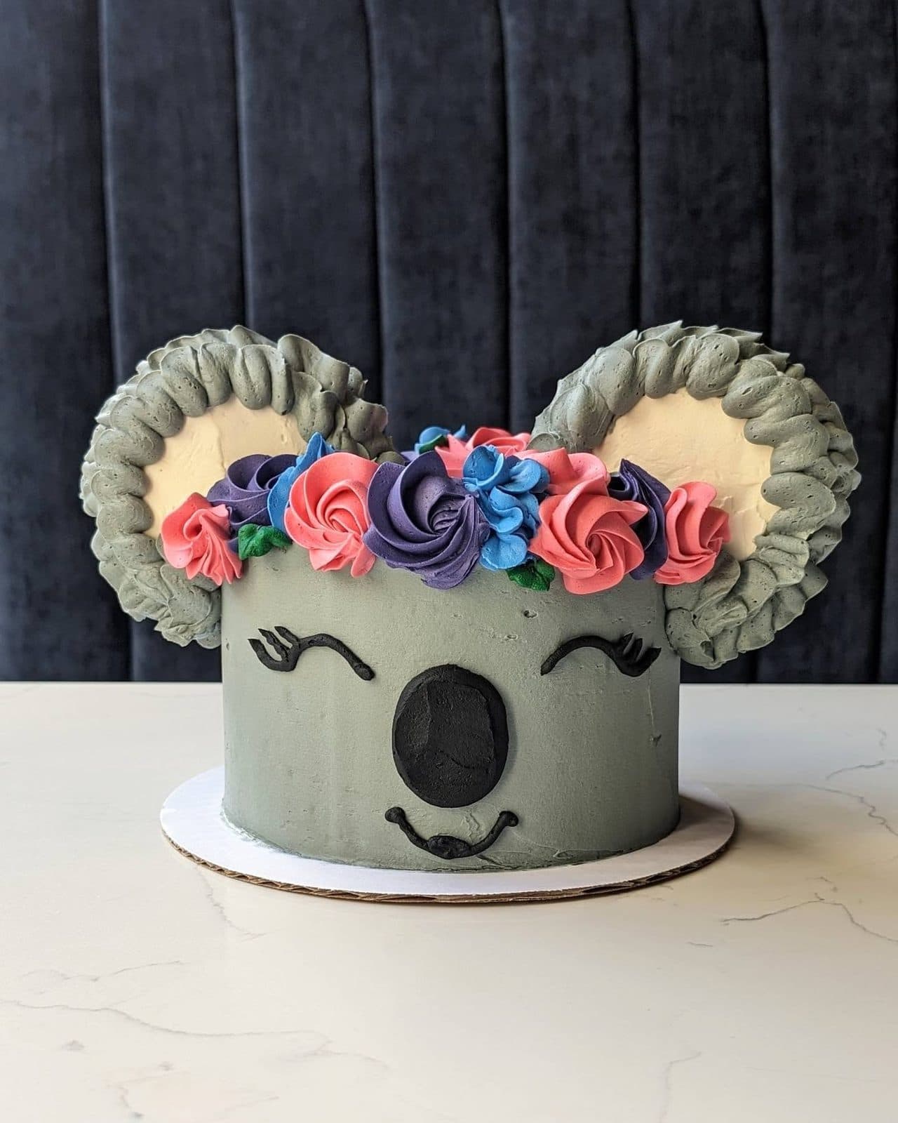 A gray buttercream koala clinging to a brown tree trunk on a smooth sage-green cake.