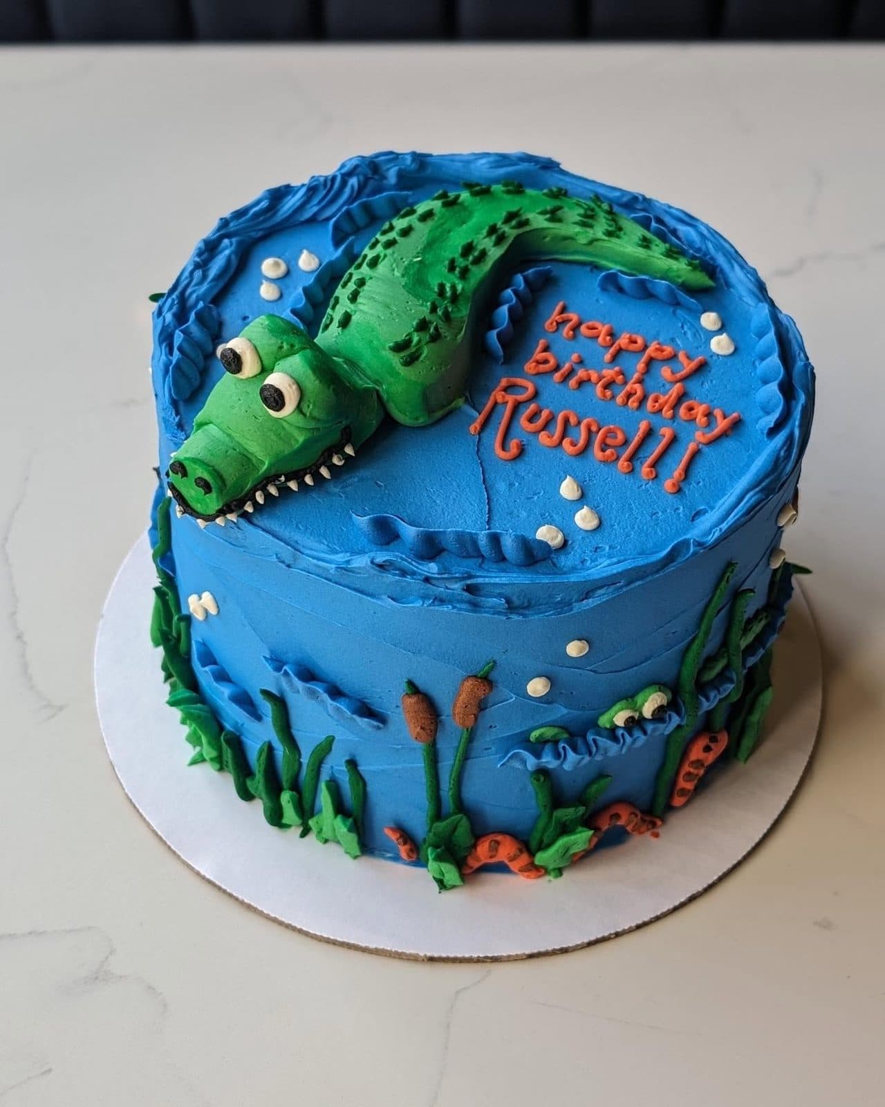 Close-up of a bright blue buttercream alligator, mouth open in rows of pointed white teeth.