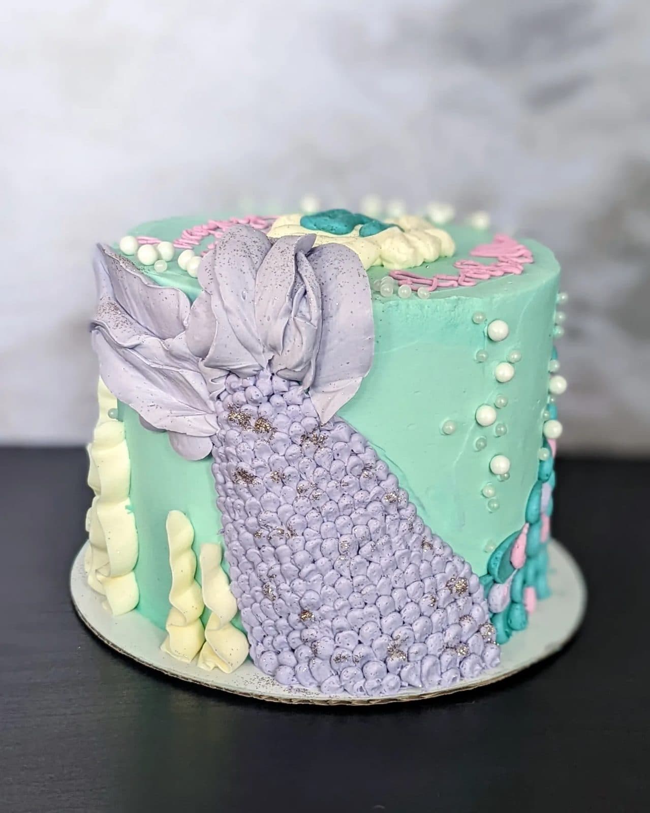 Top of the mermaid cake: swirled blue waves, a shell, and tiny white pearls.