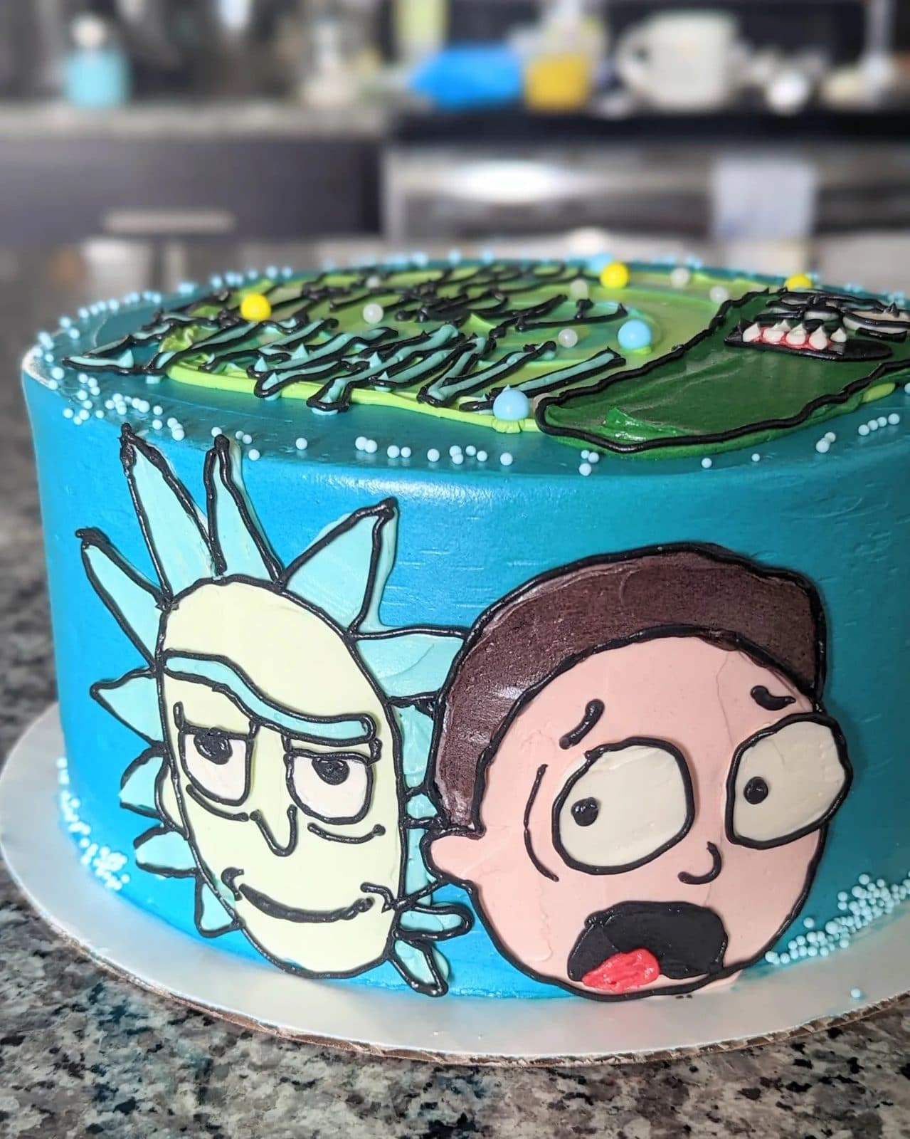 Another countertop cake, with bottles of food dye, piping tips, and a mug of coffee visible behind it.