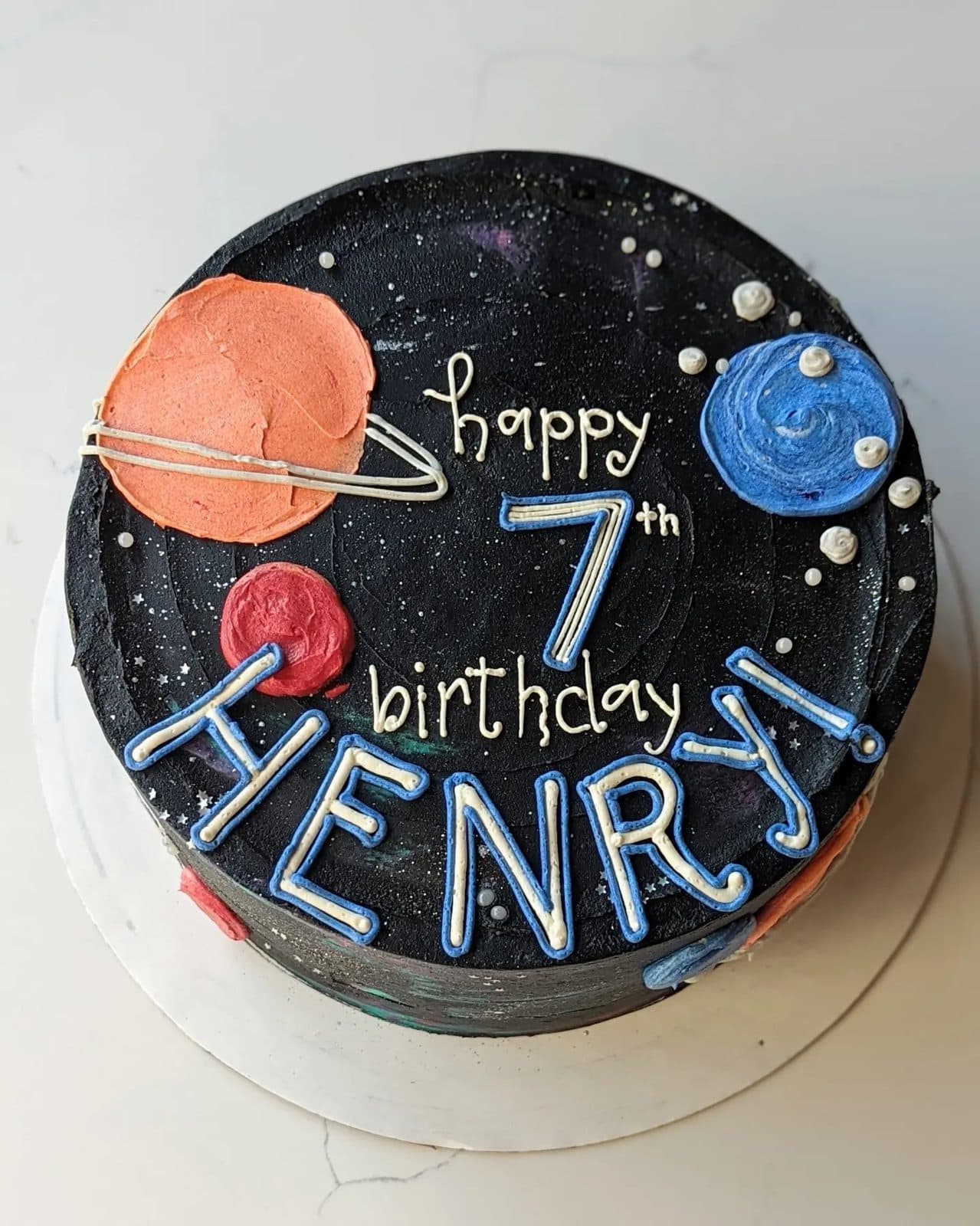 The top of the cake: planets, stars, the astronaut, and the rainbow against pale frosting.