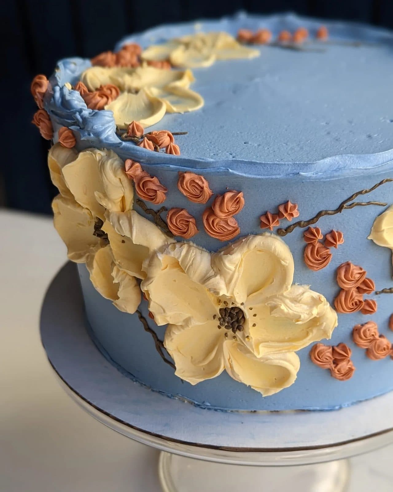 A pale blue cake covered in large piped buttercream flowers in pink, white, and periwinkle.