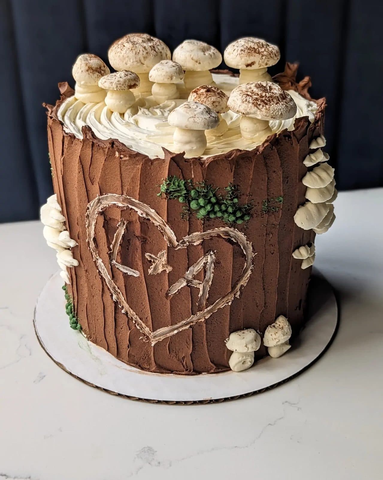 A woodland stump cake with bark-textured brown buttercream, red-capped mushrooms, moss, and tiny white flowers.