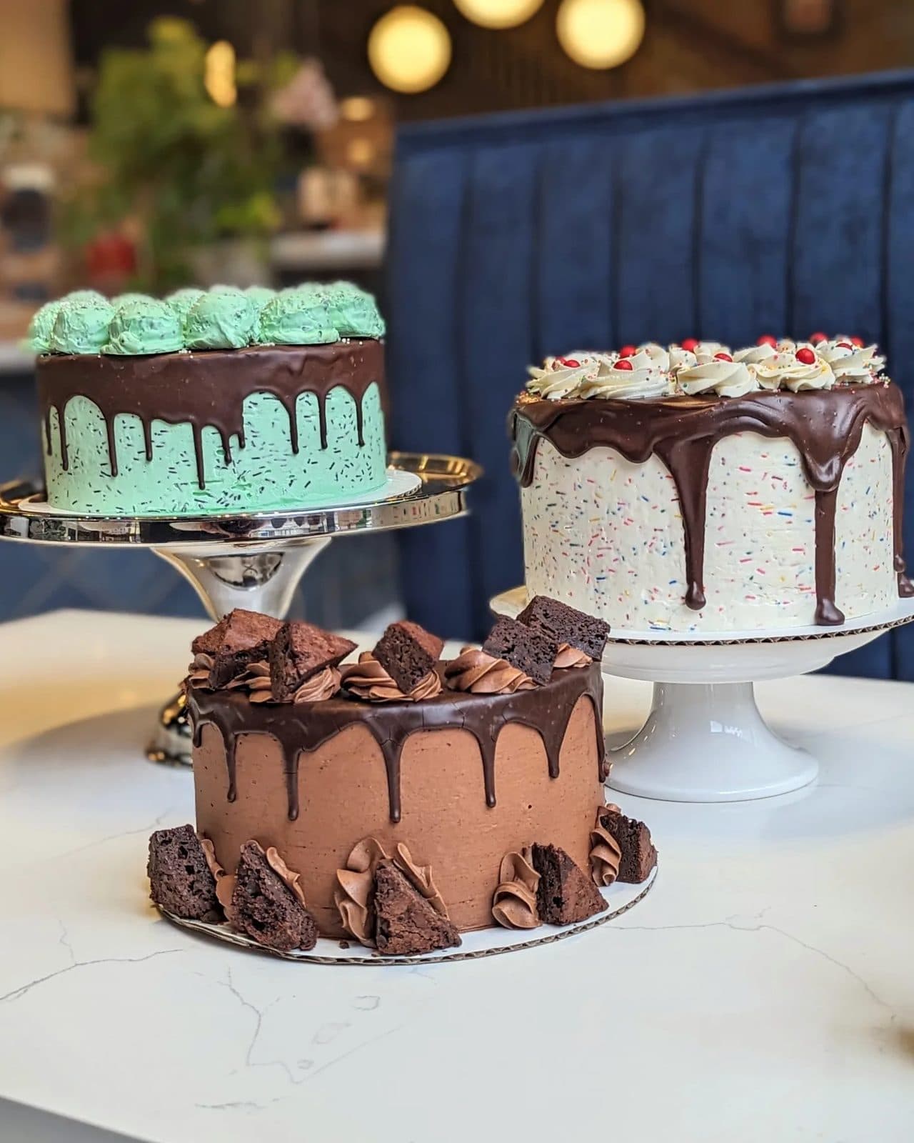 Three ice-cream-inspired cakes: mint chip with three frosting scoops, a chocolate fudge brownie cake, and a pink-and-white Neapolitan cake.
