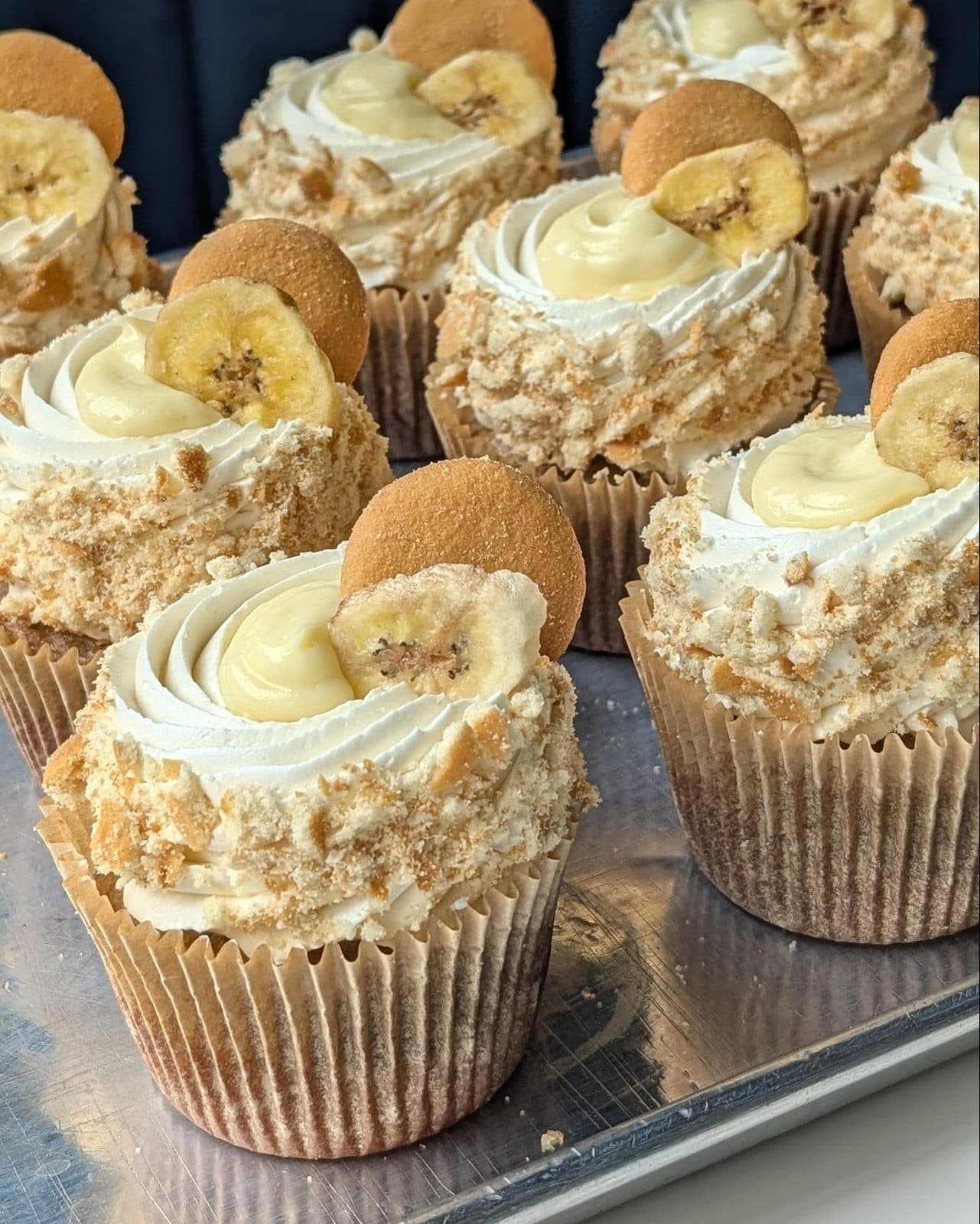 A giant cupcake in a striped liner, vanilla cake under a tall swirl of banana-pudding buttercream, vanilla wafers, and a banana slice.